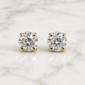 10K yellow gold 4mm round CZ stud earrings in polished four-prong settings on white marble surface
