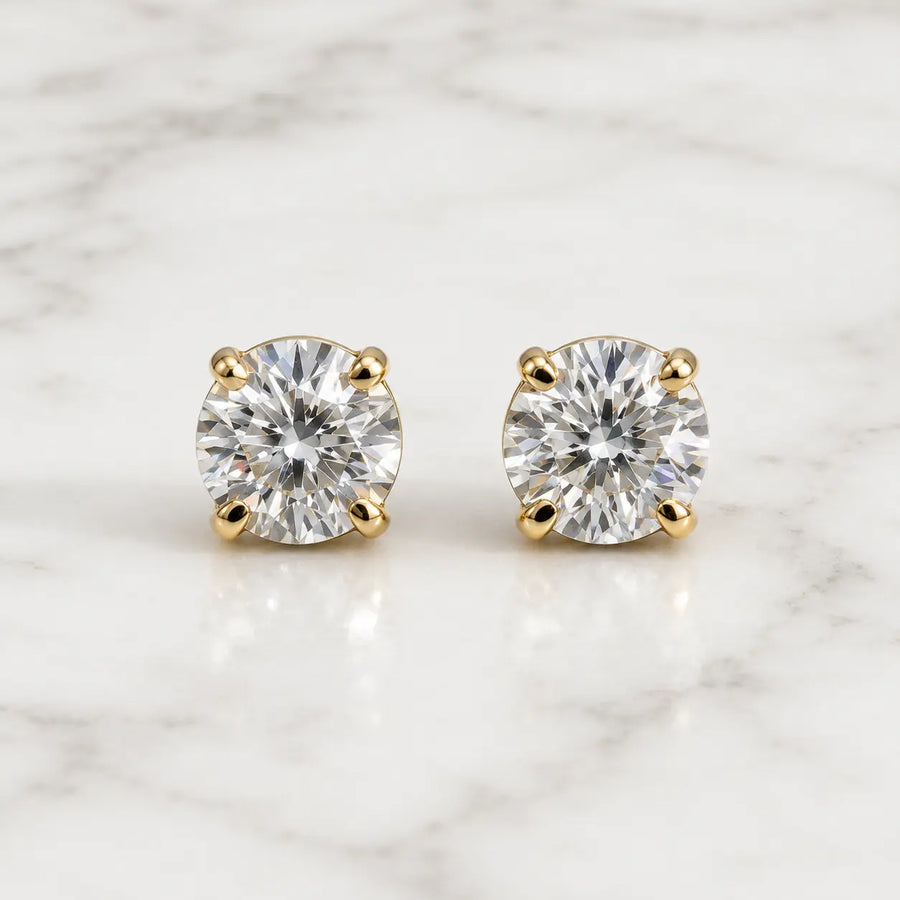 10K yellow gold 4mm round CZ stud earrings in polished four-prong settings on white marble surface