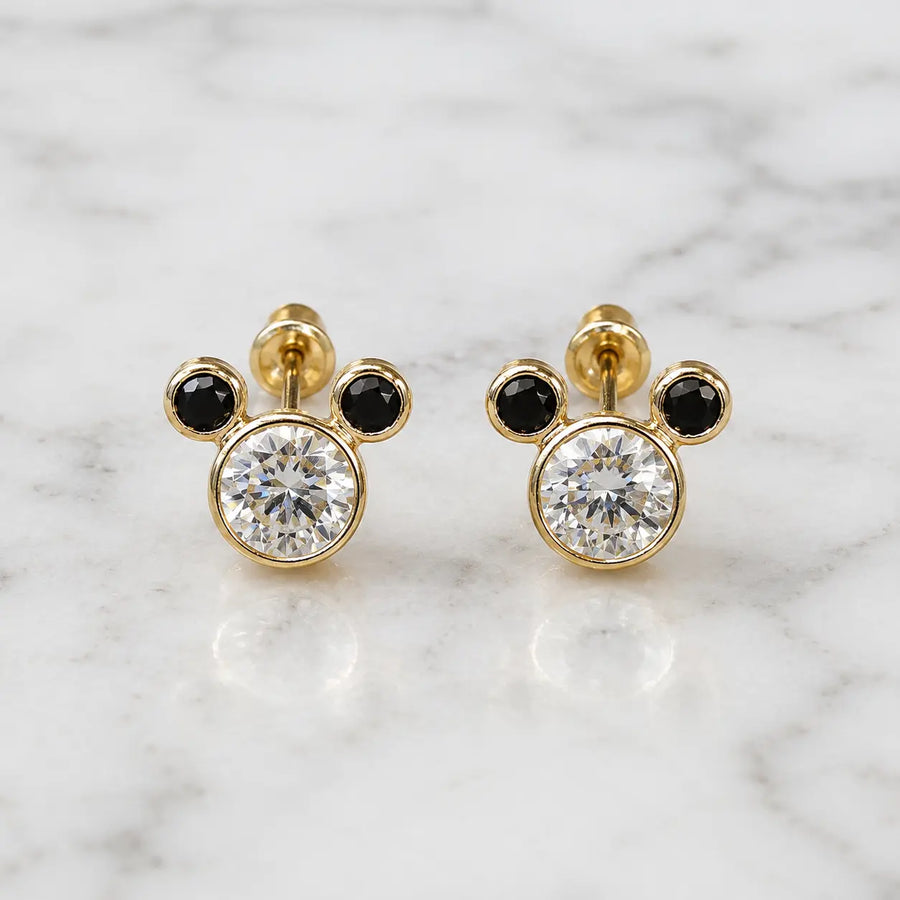 14K yellow gold mouse ear stud earrings with clear and black CZ stones on marble surface