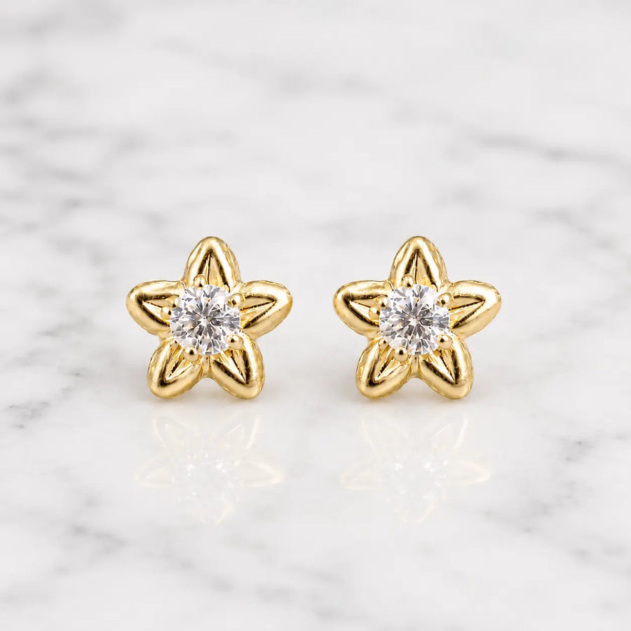 14K yellow gold CZ flower stud earrings with clear round center stone and polished petals on marble surface