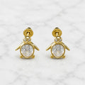 14K yellow gold penguin screw back stud earrings with clear oval CZ body on marble surface