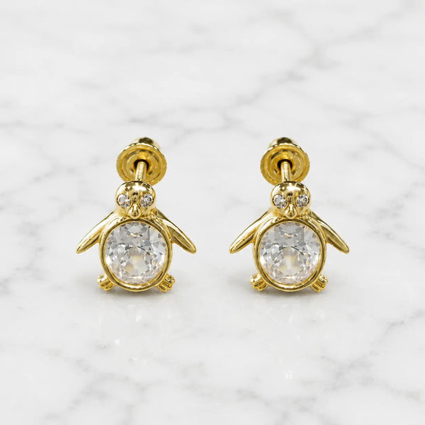 14K yellow gold penguin screw back stud earrings with clear oval CZ body on marble surface
