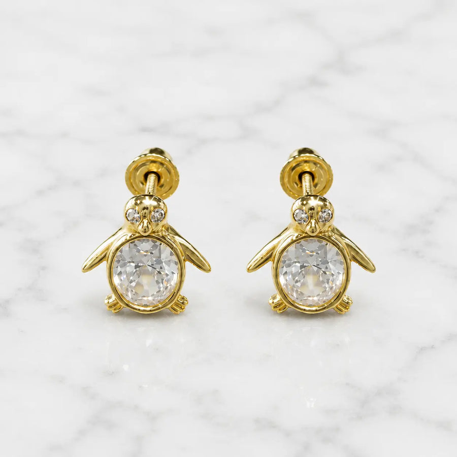 14K yellow gold penguin screw back stud earrings with clear oval CZ body on marble surface