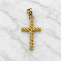 14K yellow gold cross pendant with diagonal textured detailing shown from the front on marble surface