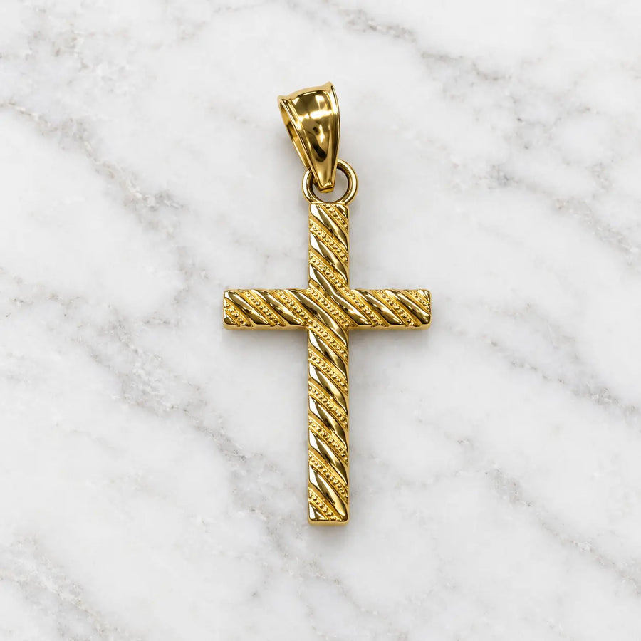 14K yellow gold cross pendant with diagonal textured detailing shown from the front on marble surface