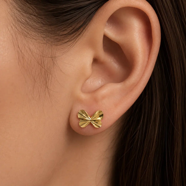 14K yellow gold diamond-cut bow stud earring worn on ear showing everyday scale and fit