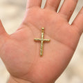 14K yellow gold diamond-cut cross pendant resting in an open palm showing its size and scale