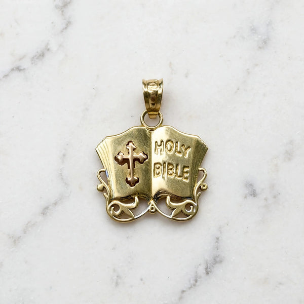 Front of a 14K yellow gold Holy Bible pendant shaped as an open book with raised HOLY BIBLE lettering, a pierced cross, and scroll filigree