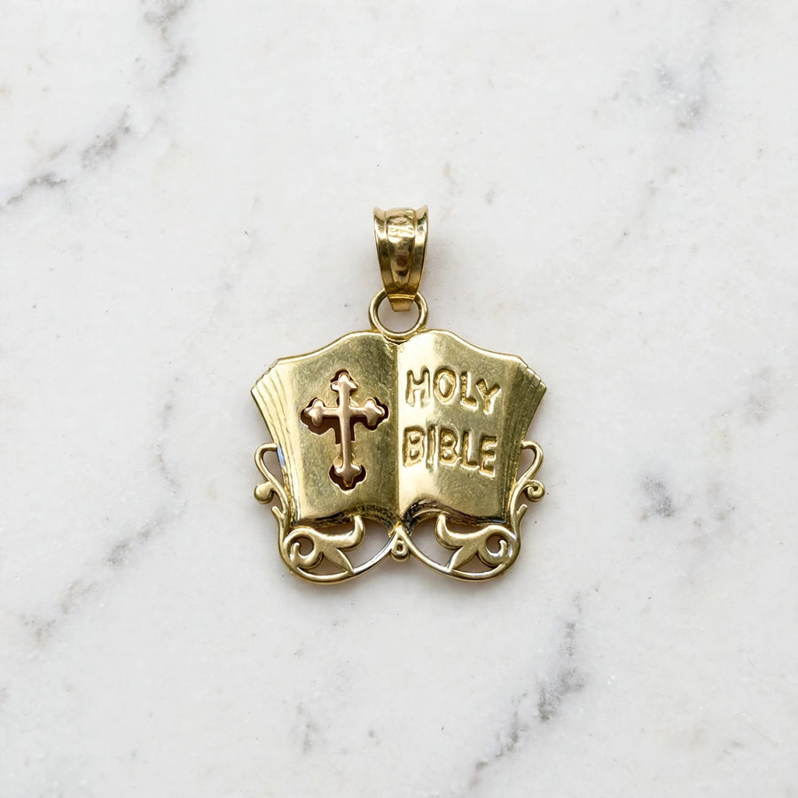 Front of a 14K yellow gold Holy Bible pendant shaped as an open book with raised HOLY BIBLE lettering, a pierced cross, and scroll filigree