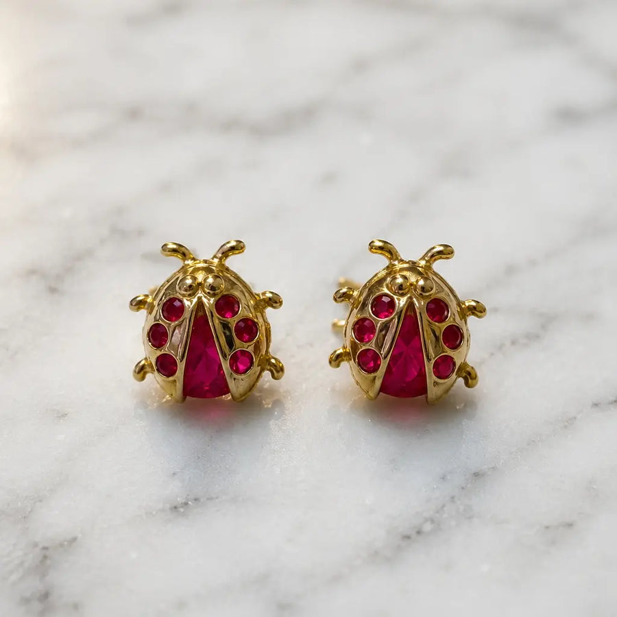 14K yellow gold ladybug stud earrings with red CZ body and wing stones shown front view on marble surface