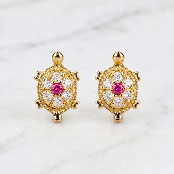 14K yellow gold turtle stud earrings with pink center CZ and clear CZ accents on marble surface