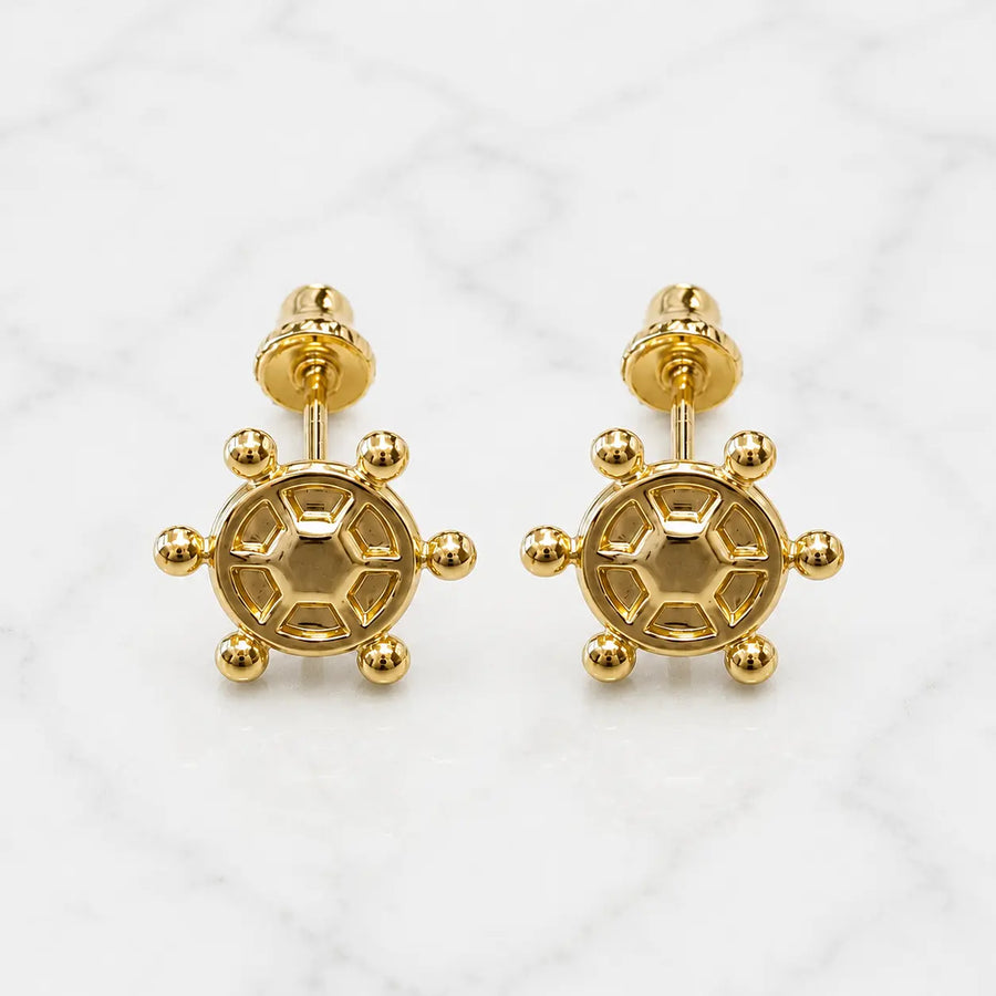14K yellow gold ship wheel screw back stud earrings with polished nautical design on marble surface