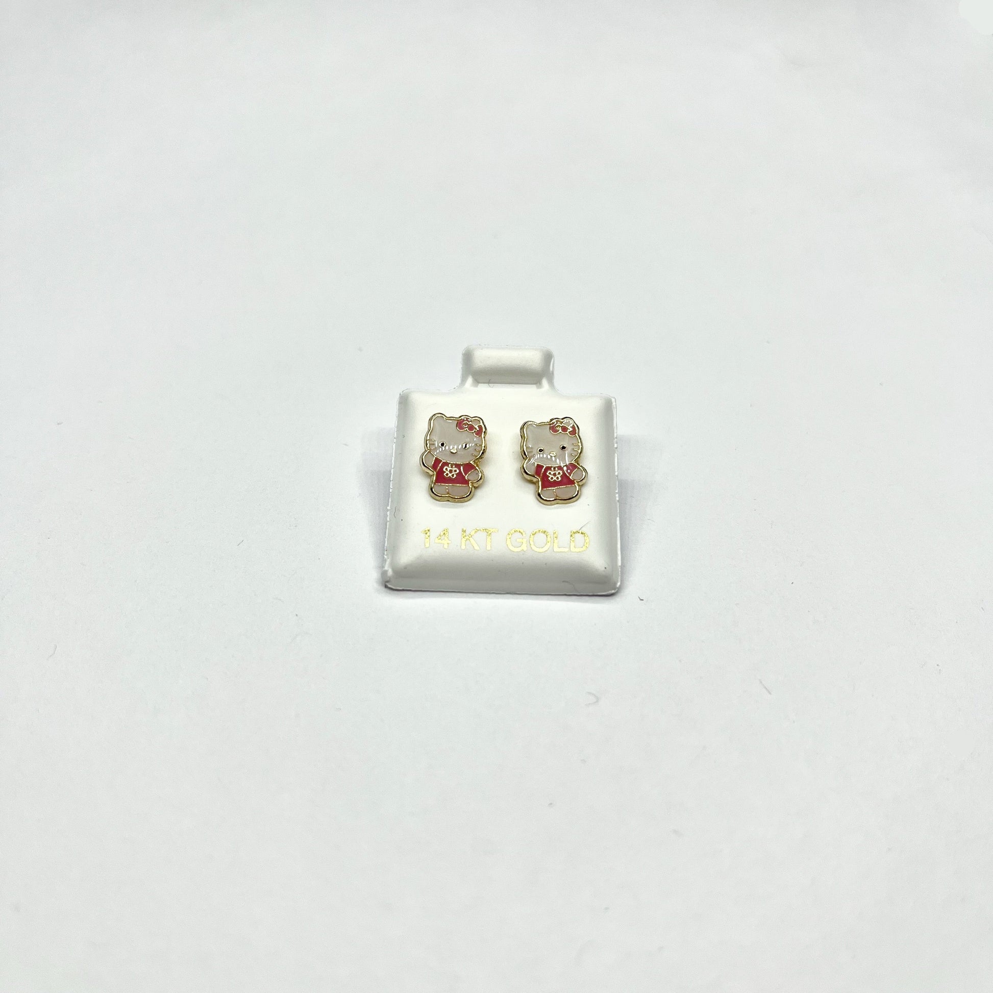 A pair of 14K gold Hello Kitty stud earrings on a white display stand.