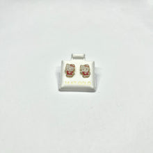 A pair of 14K gold Hello Kitty stud earrings on a white display stand.
