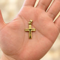 14K yellow gold polished grooved cross pendant held in an open palm showing its size and scale