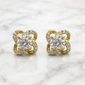 Gold tone over sterling silver 2 CTW moissanite four-petal floral stud earrings on marble surface