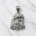 Sterling silver eagle head pendant with blue CZ eye and clear CZ accents on marble surface