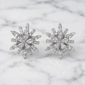Sterling silver cubic zirconia snowflake starburst stud earrings with brilliant multi-cut stones on marble surface
