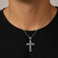 A silver crucifix pendant necklace worn by a man in a black t-shirt. The pendant features a detailed depiction of Jesus Christ on a textured cross with a polished bail, suspended from a delicate silver chain.
