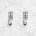 Sterling silver double row CZ huggie earrings with hinged hoop design on marble surface