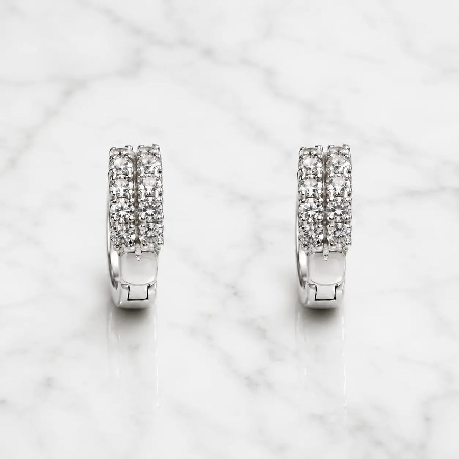 Sterling silver double row CZ huggie earrings with hinged hoop design on marble surface