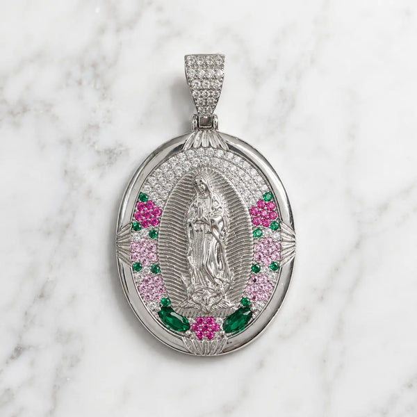 An oval silver pendant featuring a central silver figure, surrounded by pink and green gemstone accents, displayed on a white marble background.