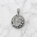 A round pavé pendant necklace featuring a panther design, set with silver-toned stones and a tiny red accent stone, displayed on a white marble background.