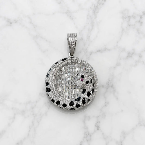 A round pavé pendant necklace featuring a panther design, set with silver-toned stones and a tiny red accent stone, displayed on a white marble background.