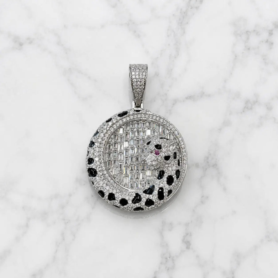 A round pavé pendant necklace featuring a panther design, set with silver-toned stones and a tiny red accent stone, displayed on a white marble background.