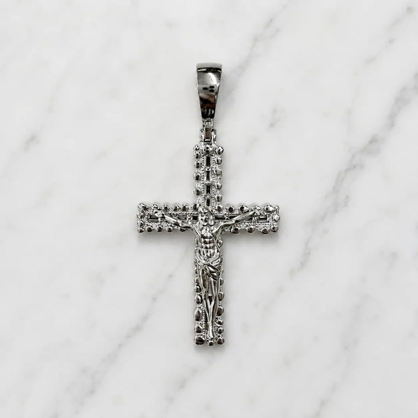 Sterling silver ornate crucifix pendant front view with raised Jesus figure and decorative border on white marble surface