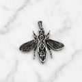 A silver insect pendant shaped like a bee or wasp, featuring detailed textured wings and body patterns, displayed on a white marble surface.