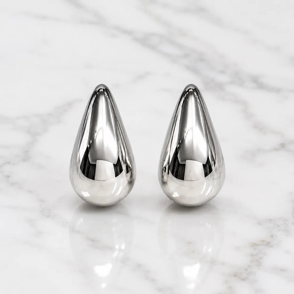 Sterling silver polished teardrop stud earrings front view with mirror-finish dome on marble surface