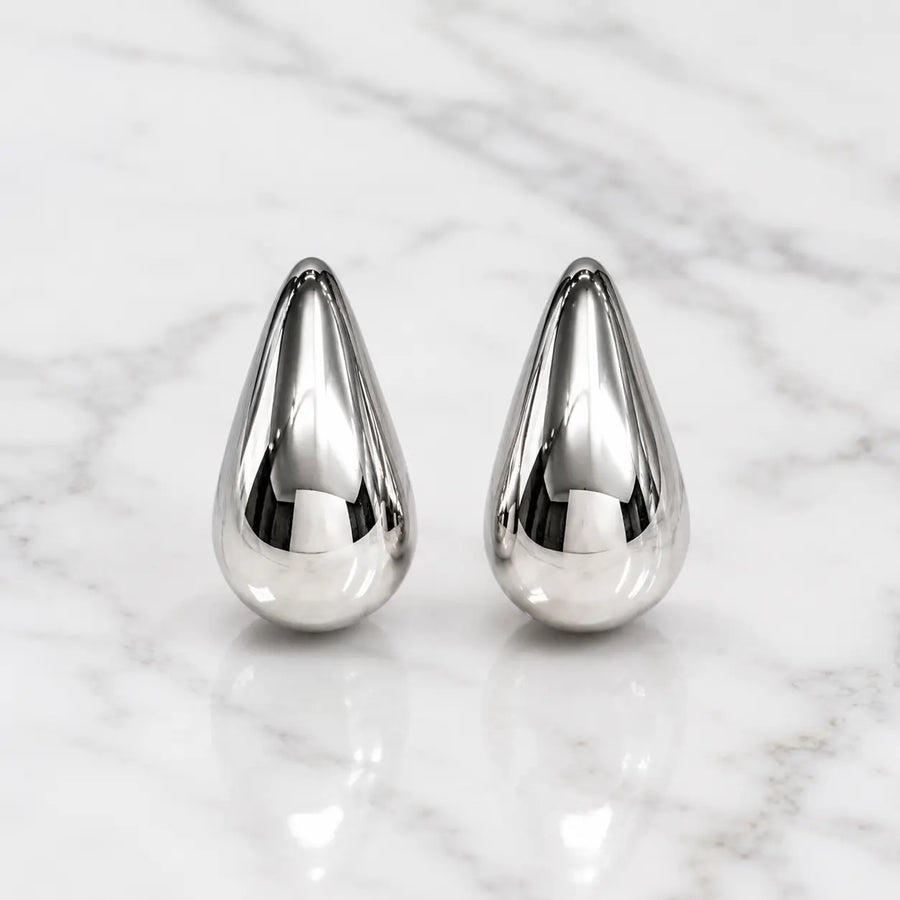 Sterling silver polished teardrop stud earrings front view with mirror-finish dome on marble surface