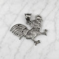 Back view of sterling silver rooster pendant showing textured detail and polished finish on marble surface