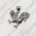 Sterling silver rooster pendant with textured feathers and red CZ eye accent on marble surface