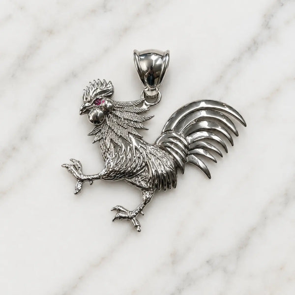Sterling silver rooster pendant with textured feathers and red CZ eye accent on marble surface