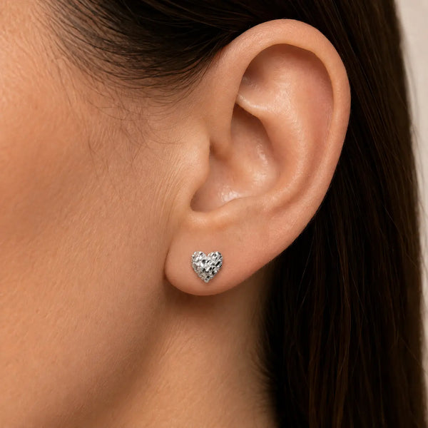 Sterling silver small diamond-cut heart stud earring worn on ear showing petite scale