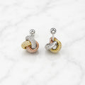 Sterling silver tri-color CZ knot stud earrings angled view with screw-back posts on marble surface